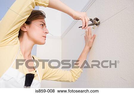 Stock Photo - Woman pulling hooks out of wall. Fotosearch