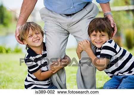 Stock Image - Boys grabbing fathers legs. Fotosearch