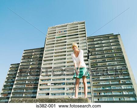 Stock Image - Woman playing golf by apartment block. Fotosearch