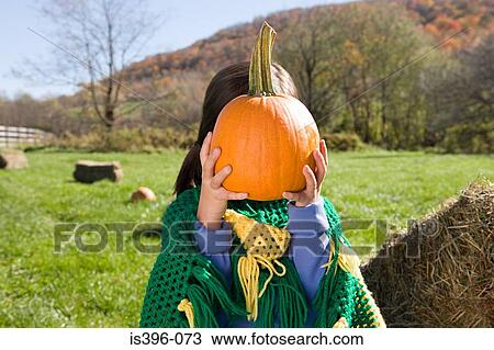 Stock Image - Girl holding pumpkin in front of her face. Fotosearch