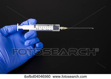 Stock Image - A hand with a blue medical glove is holding a syringe. Fotosearch