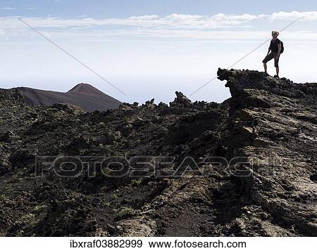 "A hiker standing on a rock in the volcanic landscape, San Antonio volcano and Teneguia volcano at the back, Los Canarios, Fuencaliente, La Palma, Canary Islands, Spain, Europe" View Large Photo Image Stock Photo - "A hiker standing on a rock in the volcanic landscape, San Antonio volcano and Teneguia volcano at the back, Los Canarios, Fuencaliente, La Palma, Canary Islands, Spain, Europe". Fotosearch