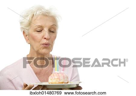 A mature woman blowing out candles on a donut View Large Photo Image Stock Photo - A mature woman blowing out candles on a donut. Fotosearch