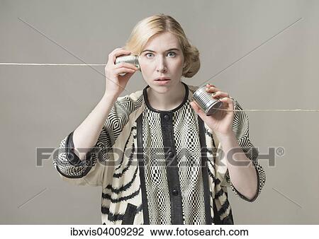 Stock Image - "Blond woman listening with tin can phone, conceptual image, spying, surveillance and communication". Fotosearch