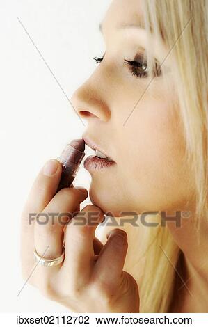 Stock Image - "Blonde young woman, applying lipstick, beauty portrait". Fotosearch