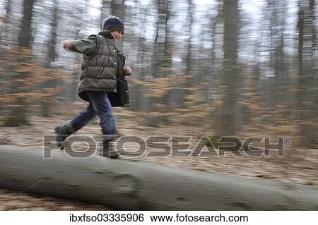 Stock Photograph - "Boy, 7 years, running over a tree trunk in a forest, Thuringia, Germany, Europe". Fotosearch