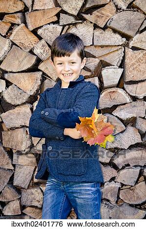"Boy holding autumn leaves, standing in front of stacked firewood" View Large Photo Image Stock Photograph - "Boy holding autumn leaves, standing in front of stacked firewood". Fotosearch