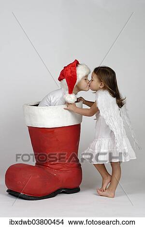 Boy in a Christmas boot and girl dressed as an angel kissing View Large Photo Image Picture - Boy in a Christmas boot and girl dressed as an angel kissing. Fotosearch