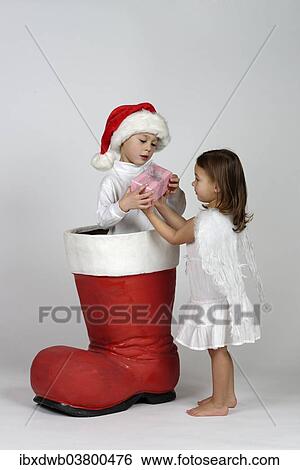 Boy in a Christmas boot handing a small Christmas present to a girl dressed as an angel View Large Photo Image Stock Photograph - Boy in a Christmas boot handing a small Christmas present to a girl dressed as an angel. Fotosearch