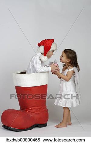 Stock Photography - Boy in a Christmas boot handing a small Christmas present to a girl dressed as an angel. Fotosearch