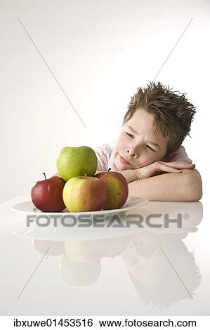 "Boy sitting in front of a plate of apples, looking skeptical" View Large Photo Image Stock Photograph - "Boy sitting in front of a plate of apples, looking skeptical". Fotosearch