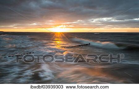Stock Image - "Breakwaters or groynes, sunset, storm clouds, breaking wave, evening light, Baltic Sea, Fischland-Darss-Zingst peninsula, Mecklenburg-Western Pomerania, Germany, Europe". Fotosearch
