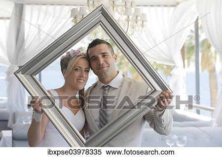 "Bride and groom holding a picture frame in front of them and looking through it, photo shoot" View Large Photo Image Stock Photography - "Bride and groom holding a picture frame in front of them and looking through it, photo shoot". Fotosearch