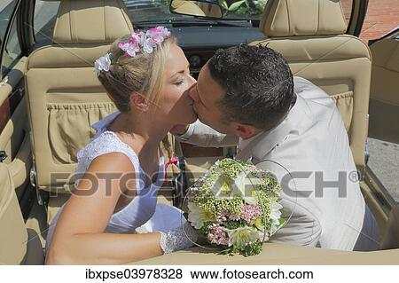 Stock Photo - "Bride and groom kissing in the back seat of an open car, convertible". Fotosearch