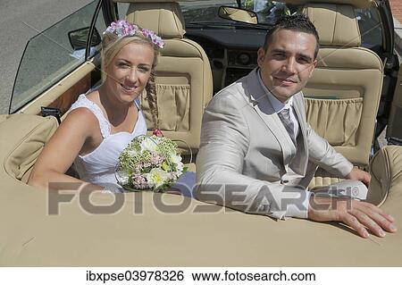 Stock Photograph - "Bride and groom posing in the back seat of an open car, convertible". Fotosearch