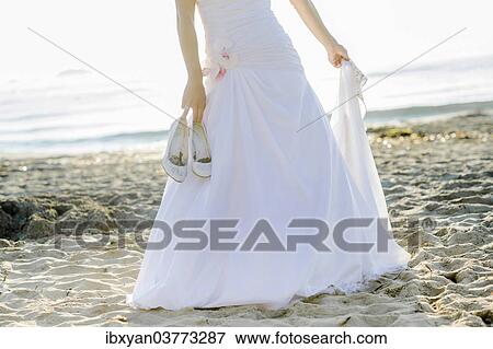 Bride carrying her shoes in her hand on a sandy beach View Large Photo Image Stock Photo - Bride carrying her shoes in her hand on a sandy beach. Fotosearch