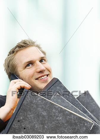 "Businessman carrying ring binders while using a mobile phone, smiling" View Large Photo Image Stock Image - "Businessman carrying ring binders while using a mobile phone, smiling". Fotosearch