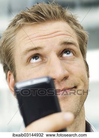 Stock Image - "Businessman holding a mobile phone, looking annoyed after receiving a SMS". Fotosearch