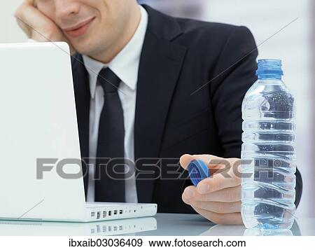 Businessman in an office with a laptop and a water bottle View Large Photo Image Stock Photo - Businessman in an office with a laptop and a water bottle. Fotosearch