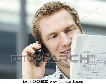 Businessman reading a newspaper while using a mobile phone View Large Photo Image Stock Image - Businessman reading a newspaper while using a mobile phone. Fotosearch