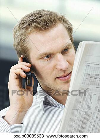 "Businessman reading a newspaper while using a mobile phone, concentrating" View Large Photo Image Stock Image - "Businessman reading a newspaper while using a mobile phone, concentrating". Fotosearch