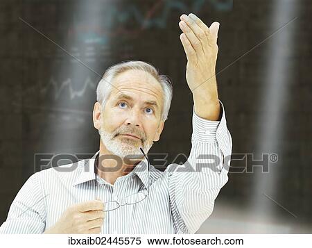 "Businessman, senior, with a serious expression and holding a pair of glasses, gesticulating, at the stock exchange" View Large Photo Image Stock Photography - "Businessman, senior, with a serious expression and holding a pair of glasses, gesticulating, at the stock exchange". Fotosearch