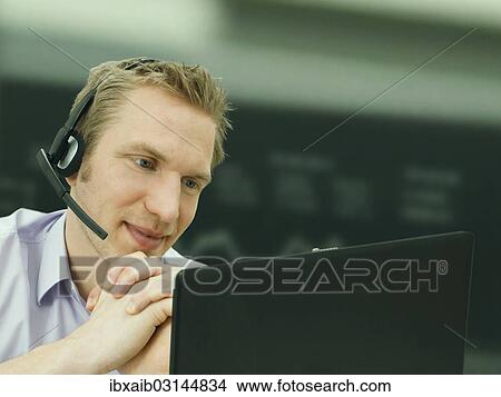 Businessman wearing a headset while working on a laptop at the stock exchange View Large Photo Image Picture - Businessman wearing a headset while working on a laptop at the stock exchange. Fotosearch
