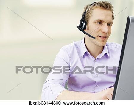 Businessman wearing a headset while working on a laptop View Large Photo Image Stock Image - Businessman wearing a headset while working on a laptop. Fotosearch