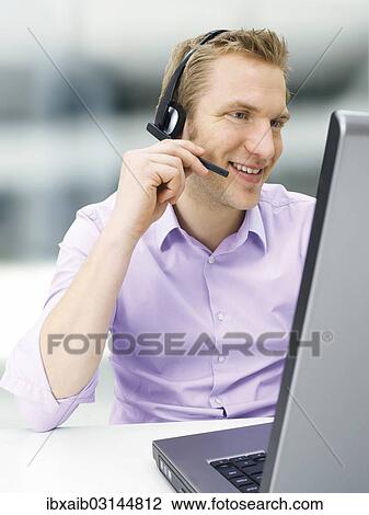 Businessman wearing a headset while working on a laptop View Large Photo Image Stock Image - Businessman wearing a headset while working on a laptop. Fotosearch