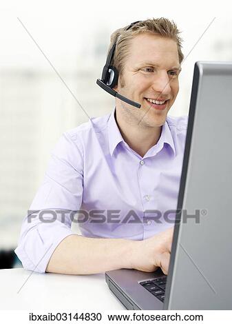 Businessman wearing a headset while working on a laptop View Large Photo Image Stock Image - Businessman wearing a headset while working on a laptop. Fotosearch