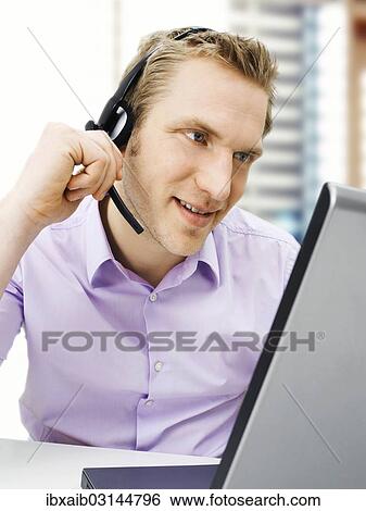 Businessman wearing a headset while working on a laptop View Large Photo Image Stock Photograph - Businessman wearing a headset while working on a laptop. Fotosearch