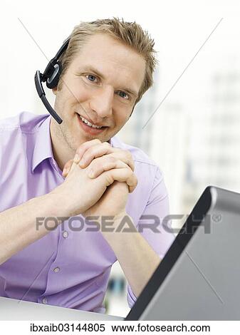 Businessman wearing a headset while working on a laptop View Large Photo Image Stock Photography - Businessman wearing a headset while working on a laptop. Fotosearch