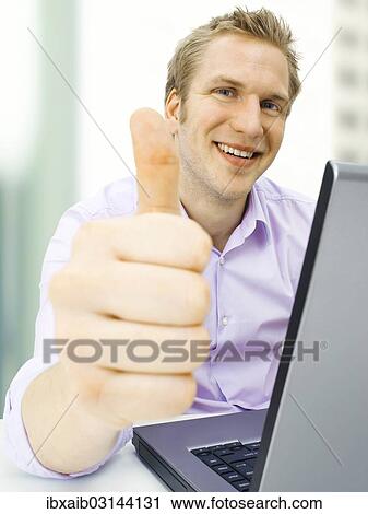 "Businessman working on a laptop, making a thumbs-up gesture" View Large Photo Image Stock Image - "Businessman working on a laptop, making a thumbs-up gesture". Fotosearch
