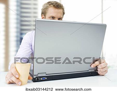 Stock Image - "Businessman working on a laptop, holding a plastic cup, concentrating". Fotosearch