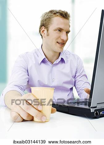 "Businessman working on a laptop, holding a plastic cup" View Large Photo Image Stock Photo - "Businessman working on a laptop, holding a plastic cup". Fotosearch