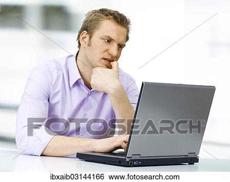 Stock Photograph - "Businessman working on a laptop, concentrating, nibbling on his fingernail". Fotosearch