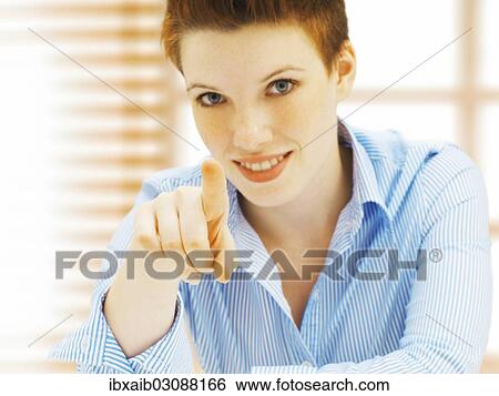 Stock Photograph - "Businesswoman in an office, smiling, pointing forward". Fotosearch