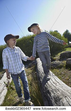 Stock Photo - Child helping another balancing on a tree trunk. Fotosearch