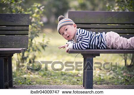 "Child lying on a bench in the park, exploring" View Large Photo Image Stock Photo - "Child lying on a bench in the park, exploring". Fotosearch