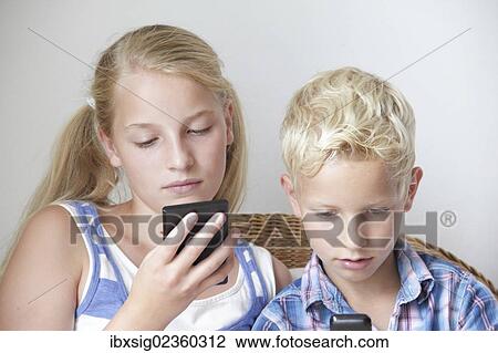 Stock Image - Children looking at their mobile phones. Fotosearch