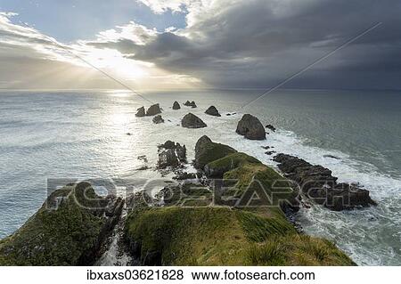 Stock Photo - "Cliffs rising from the Pacific with a rising sun, at Nugget Point, Nugget Point, Ahuriri Flat, Otago Region, New Zealand, Oceania". Fotosearch
