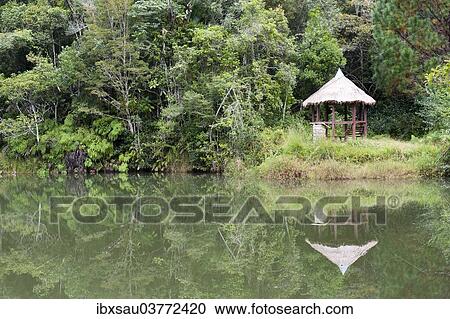 Stock Image - "Cottage reflected in a lake, jungle, primary forest, Andasibe-Mantadia National Park, Alaotra Mangoro region, Madagascar, Africa". Fotosearch