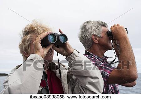 "Couple, 60-65 years, using binoculars, Northumberland, England, United Kingdom, Europe" View Large Photo Image Stock Photo - "Couple, 60-65 years, using binoculars, Northumberland, England, United Kingdom, Europe". Fotosearch