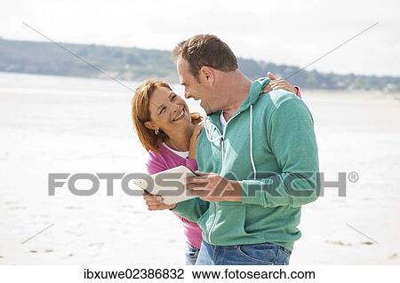 Stock Image - Couple playing with a digital tablet on a beach. Fotosearch