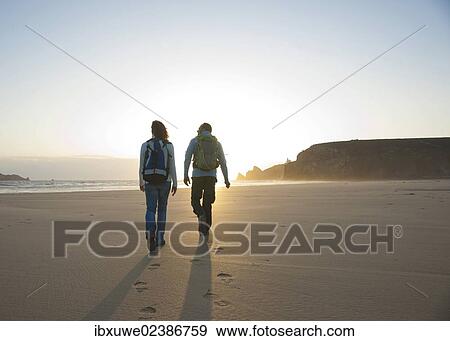 Couple walking along the beach towards the sunset View Large Photo Image Stock Photo - Couple walking along the beach towards the sunset. Fotosearch