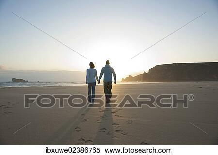 Couple walking along the beach towards the sunset View Large Photo Image Stock Photography - Couple walking along the beach towards the sunset. Fotosearch
