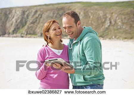 Couple with a digital tablet on a beach View Large Photo Image Stock Photo - Couple with a digital tablet on a beach. Fotosearch