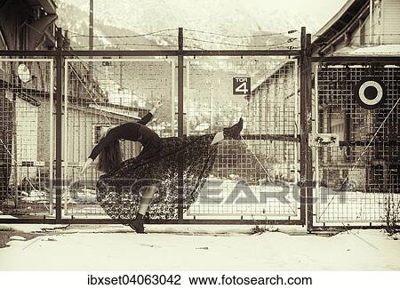 Stock Image - "Dancer in a black dress performing in front of an old fence in winter, Innsbruck, Tyrol, Austria, Europe". Fotosearch