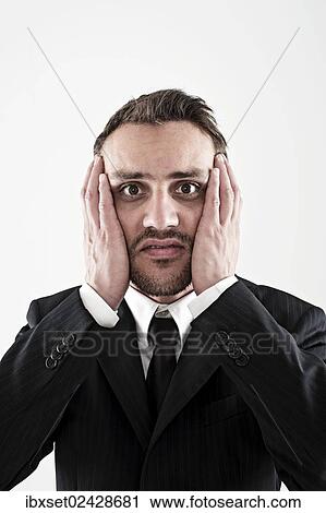 Stock Image - "Desperate young man wearing a suit holding his hands to his face, worried". Fotosearch