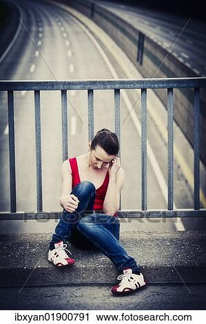 Stock Image - Desperate young woman sitting at a highway bridge. Fotosearch